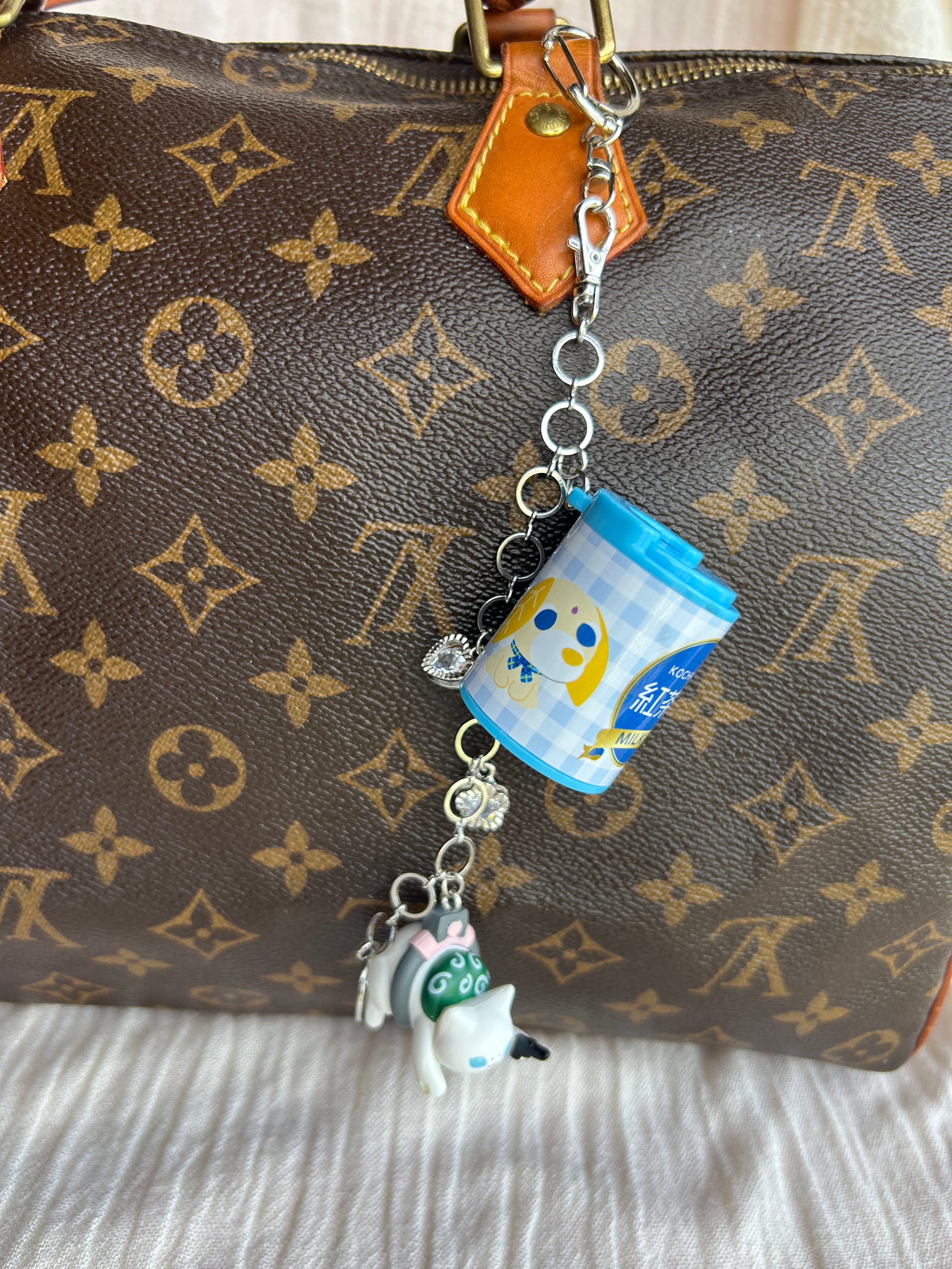 A close-up of a brown Louis Vuitton monogram bag with a silver-tone keychain charm featuring a blue cup character and a small white dog charm.